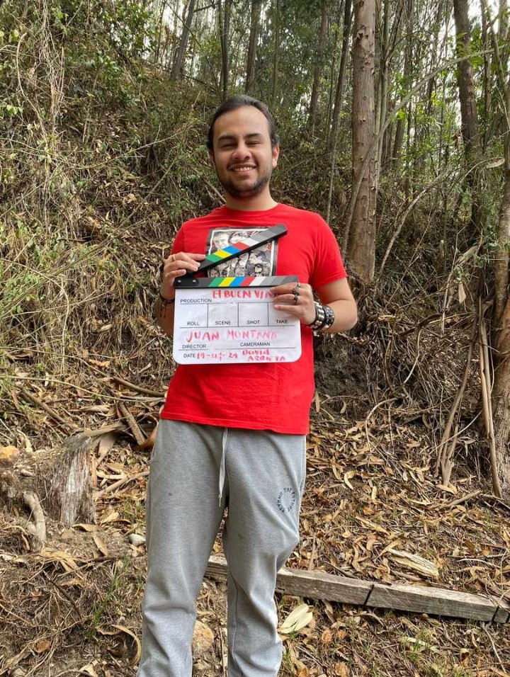 Juan Camilo Montaña está de pie dirigiendo su cuerpo hacia la cámara. Tiene una camisa roja y en sus manos la claqueta, el dispositivo liviano, de acrílico y rectangular sobre el cual se escriben los datos de la fecha, plano y escena de una obra audiovisual. Al chocar la barra superior con la inferior suena el ¡clac! del cámara, sonido... ¡acción!