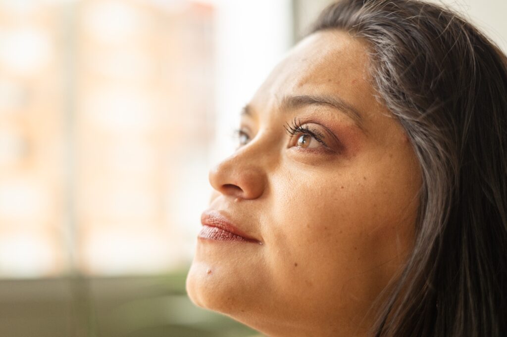 Rostro de perfil de Mónica Cortes, una mujer jóven de piel trigueña y cabello castaño que dirige su mirada hacia el cielo